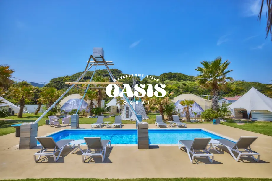 水辺と自然が響き合う、OASIS-OARAIの全景 - 茨城・大洗ひたちなかエリアのグランピング施設 Water front Villa OASIS大洗 晴天の下、OASIS-OARAIのプールとティピー・ドーム型宿泊棟が並ぶラグジュアリーな屋外空間。